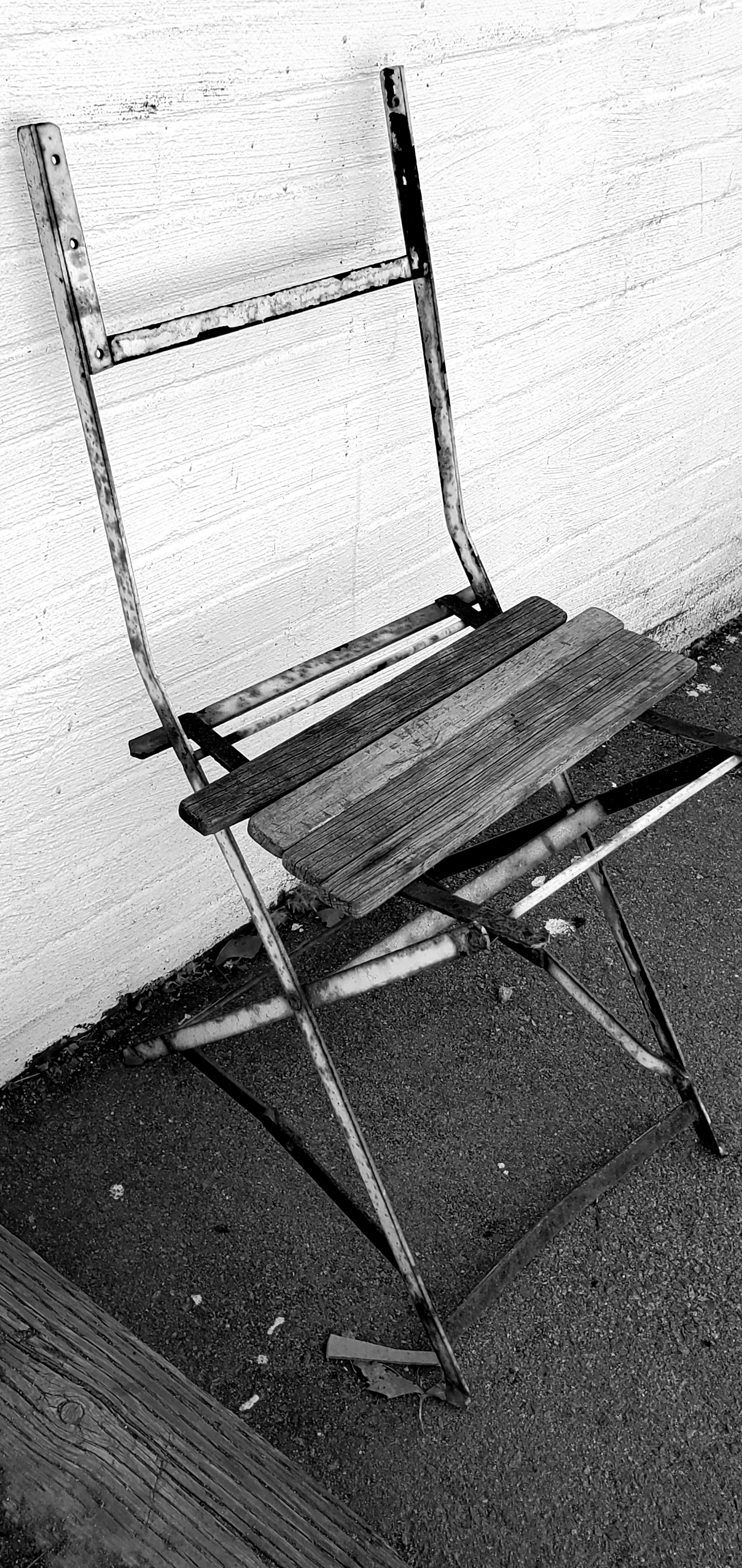 rusted metal folding chair frame with a few wooden boards across the seat